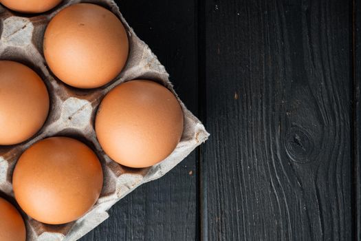 Chicken eggs in an egg box tray set, on black wooden table background, top view flat lay , with space for text copyspace