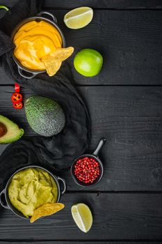 Green guacamole and yellow cheese dip sauce for traditional, Mexican tacos, on black wooden background, top view or flat lay with copy space for text