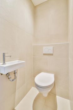 Wall hung toilet and small sink in corner in lavatory room with beige tile