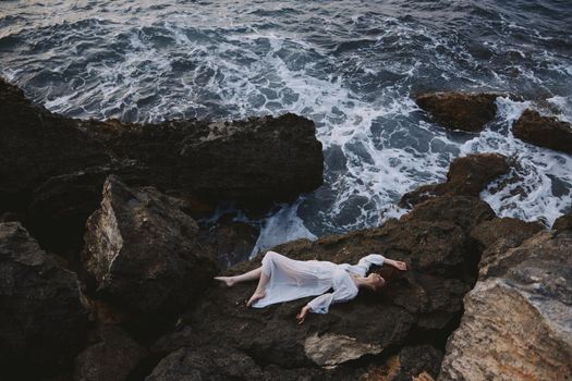Beautiful bride in long white dress wet hair lying on a rocky cliff unaltered. High quality photo