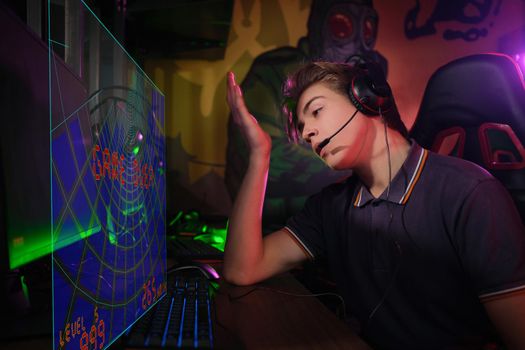 Photo of professional young caucasian gamer playing online on his PC in gaming club or cyber arena. He looks displeased and upset. Game plan went wrong. laser screen, projector, augmented reality, AR, VR