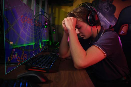 Photo of professional young caucasian gamer playing online on his PC in gaming club or cyber arena. He looks displeased and upset. Game plan went wrong. laser screen, projector, augmented reality, AR, VR