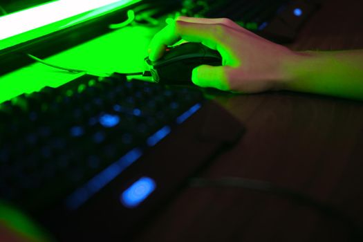 Close up view of professional players hands on gaming mouse in gaming club or cyber arena. Green neon light