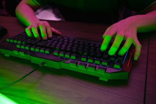 Close up view of professional players hands on gaming keyboard in gaming club or cyber arena. Green neon light