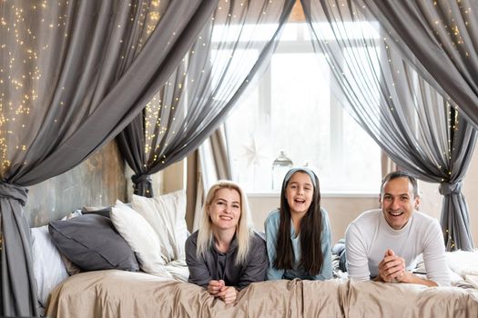 Top view of beautiful young mother, father and their daughter smiling while lying on bed.