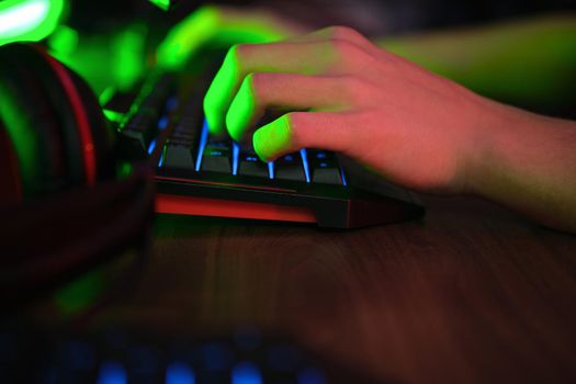 Close up view of professional players hands on gaming keyboard in gaming club or cyber arena. Green neon light