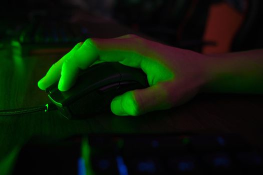 Close up view of professional players hands on gaming mouse in gaming club or cyber arena. Green neon light