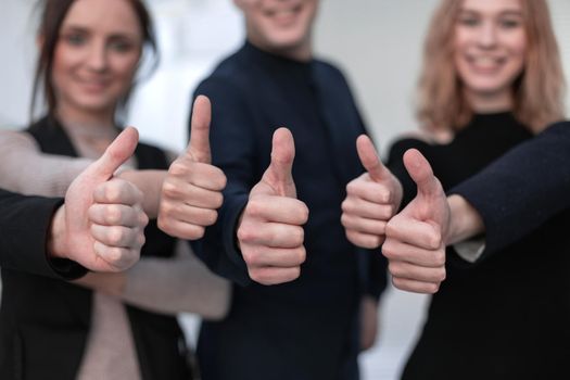 Close-up of group of business people raising their arms up and showing thumbs up