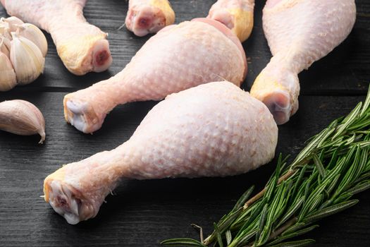 Raw uncooked chicken legs, drumsticks set, with seasoning and herbs rosemary and thyme, on black wooden table background