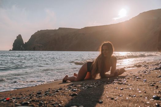 Selective focus. Happy carefree sensual woman with long hair in black swimwear posing at sunset beach. Silhouette of young beautiful playful positive woman outdoor. Summer vacation and trip concept.