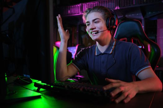 Photo of professional young caucasian gamer playing online on his PC in gaming club or cyber arena. He looks displeased and upset. Game plan went wrong