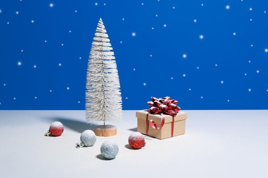 Beautiful Christmas or New Year banner with copy space. Toy Christmas tree, gift box with red bow and Christmas baubles on blue background with snow falling on the background