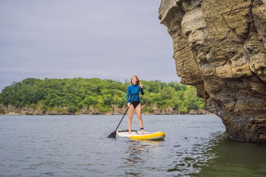 Young women Having Fun Stand Up Paddling in the sea. SUP. Red hair girl Training on Paddle Board near the rocks.