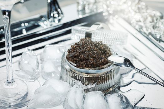 Black caviar. Black sturgeon caviar in a cut-glass bowl and a metal spoon on a silver tray.
