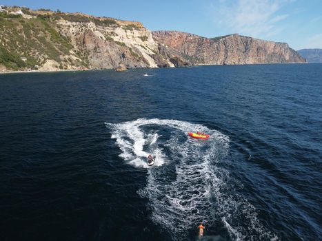 Inflatable attraction. Happy people are going to swim on an air mattress behind a jet ski. Tourists ride the inflatable watercraft boat. Jet ski skating people on a large Inflatable raft