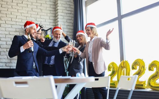 Business people are celebrating holiday in modern office drinking champagne and having fun in coworking. Merry Christmas and Happy New Year 2022