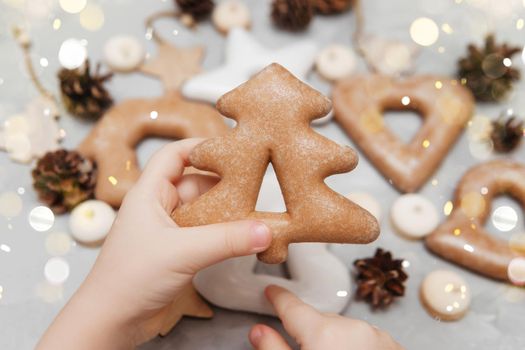 Children's hands hold a gingerbread in the shape of a Christmas tree. The concept of Christmas sweets, toys, garlands and bokeh. Decor for New Year holidays.