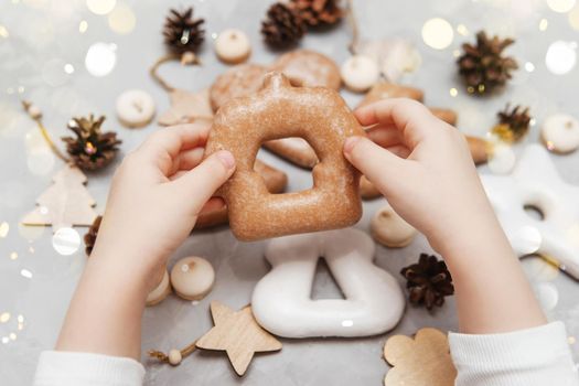 Children's hands hold a gingerbread in the shape of a home. The concept of Christmas sweets, toys, garlands and bokeh. Decor for New Year holidays.