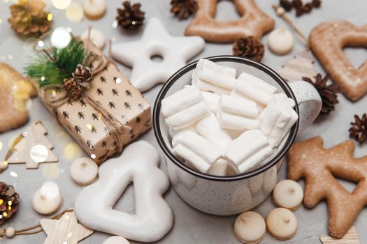 A cup of cocoa with marshmallows and New Year's gingerbread and a gift on the table, bokeh lights in the foreground. The concept of desserts and drinks during the Christmas holidays.