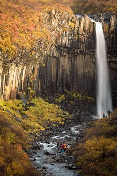 Svartifoss waterfall silk water with unrecognizable tourists on autumn