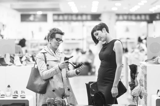 Two Girl-Friends On Shopping Walk On Shopping Centre With Bags And Choosing