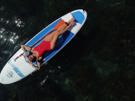 Young attractive brunette woman in red swimsuit, swimming on kayak around volcanic rocks, like in Iceland. Back view. Christmas holiday vacation and travel concept.