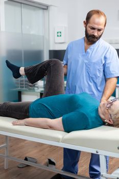 Close up of chiropractor giving assistance to senior patient with knee injury for physical recovery. Woman doing leg exercise with help from medical assistant for osteopathic remedy.