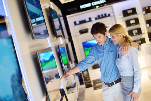 Young couple in consumer electronics store looking at latest laptop, television and photo camera