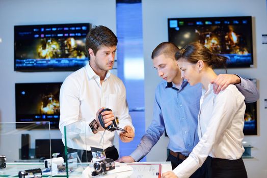 Young couple in consumer electronics store looking at latest laptop, television and photo camera to buy