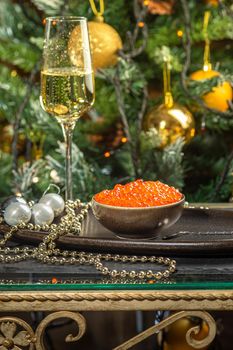 Red caviar in a a ceramic bowl, silver beads and pearls and a glass of champagne on a silver tray. Christmas and New Year background
