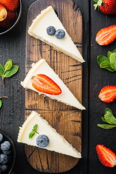 Slice of cheesecake with strawberries, blueberry and mint, on black wooden table background, top view flat lay