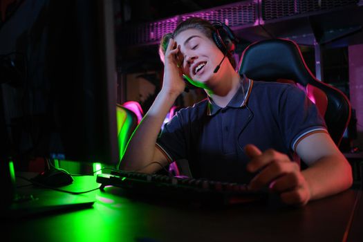 Photo of professional young caucasian gamer playing online on his PC in gaming club or cyber arena. He looks displeased and upset. Game plan went wrong