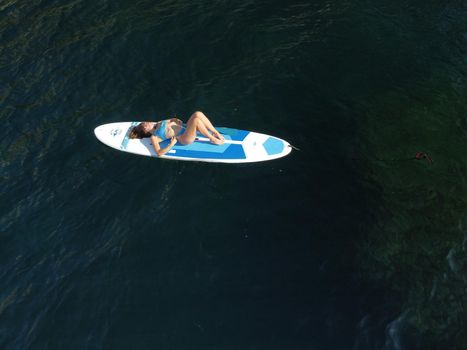 Young attractive brunette woman in red swimsuit, swimming on kayak around volcanic rocks, like in Iceland. Back view. Christmas holiday vacation and travel concept.