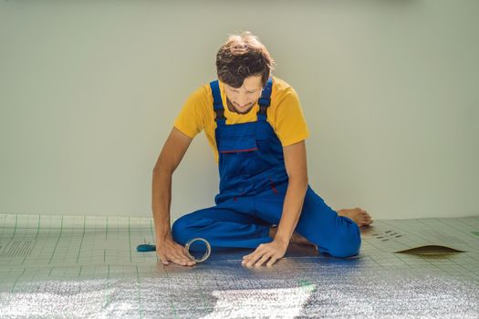 Master installs the overlapping thermal insulation in the room. Floor heating installation. Male hand holds reinforced tape. Repair in the apartment, floor insulation.