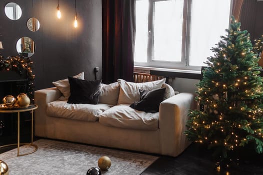 Christmas interior with a beautiful Christmas tree, sofa, light bulbs and dark background. Home New Year's interior.