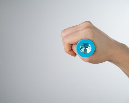 Woman holding a blue butt plug with crystal on a white background. Adult toy for alternative sex.