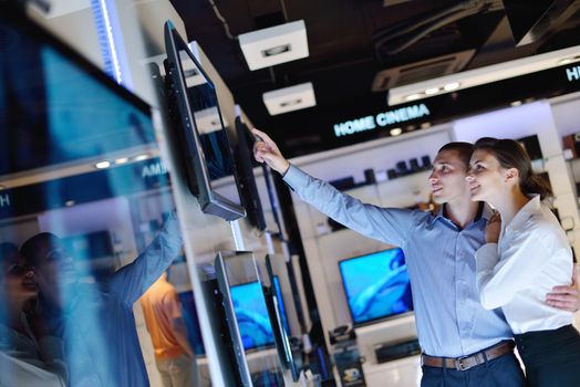 Young couple in consumer electronics store looking at latest laptop, television and photo camera to buy