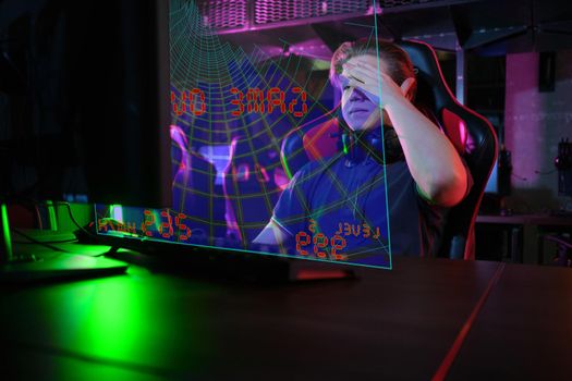 Photo of professional young caucasian gamer playing online on his PC in gaming club or cyber arena. He looks displeased and upset. Game plan went wrong. laser screen, projector, augmented reality, AR, VR