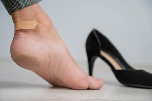 A woman in black shoes puts a plaster on a corn.