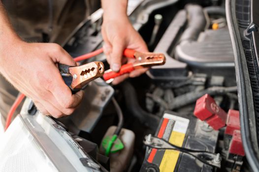 The mechanic connects the clamps to the discharged car battery