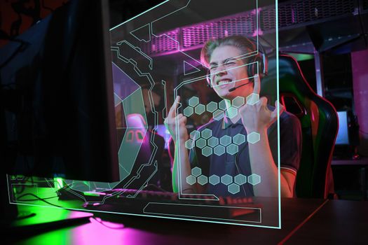 Photo of professional young caucasian gamer playing online on his PC in gaming club or cyber arena. he is upset and shows rude gestures to his virtual opponents. laser screen, projector, augmented reality, AR, VR