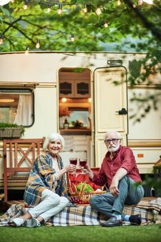 Full length photo of senior man and woman celebrating with red wine while clinking their glasses and toasting. Travel concept