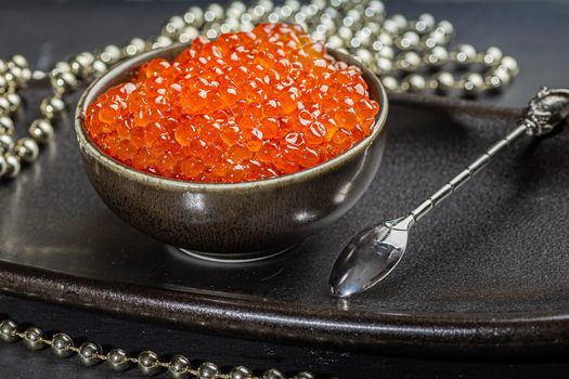 Red caviar in a a ceramic bowl, silver beads and pearls on a silver tray. Christmas and New Year background