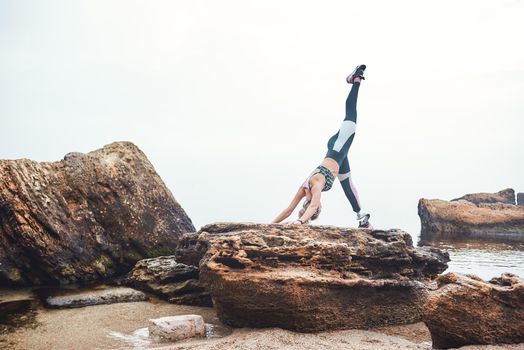 Yoga in the morning. Healthy and sporty disabled athlete woman in sportswear with prosthetic leg standing doing yoga on the stone in front of the sea. Sport concept. Disabled Sportsman. Healthy lifestyle