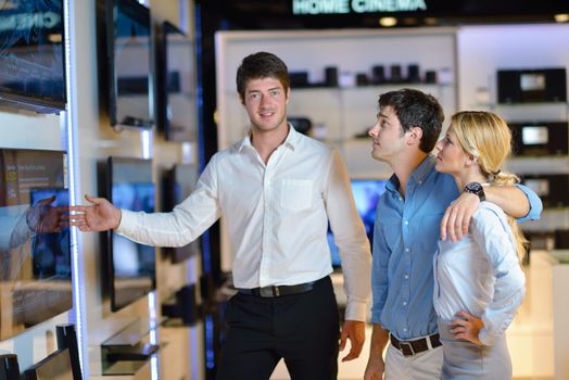 Young couple in consumer electronics store looking at latest laptop, television and photo camera