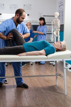 Chiropractor trying to relieve pressure from knee of patient with arthritis and pain. Medical assistant cracking leg bones for relief and physical recovery of retired woman with ache.