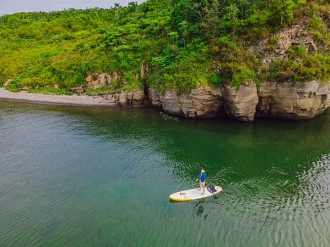 Young women Having Fun Stand Up Paddling in the sea. SUP. Red hair girl Training on Paddle Board near the rocks.