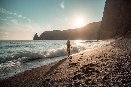 Selective focus. Happy carefree sensual woman with long hair in black swimwear posing at sunset beach. Silhouette of young beautiful playful positive woman outdoor. Summer vacation and trip concept.