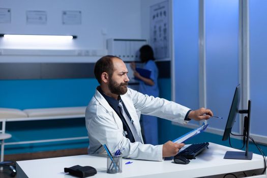 Concentated physician pointing at monitor for examination work at night shift. Doctor looking at computer screen for analysis information and healthcare. Medical specialist working late