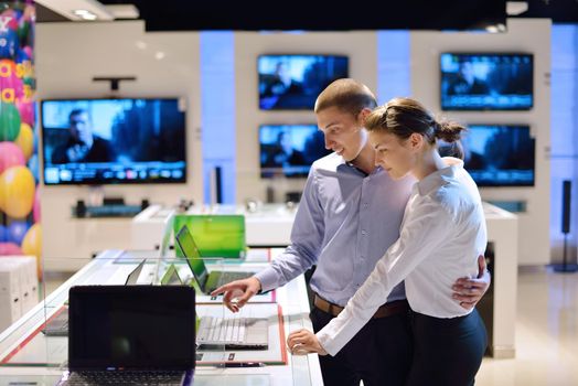 Young couple in consumer electronics store looking at latest laptop, television and photo camera to buy